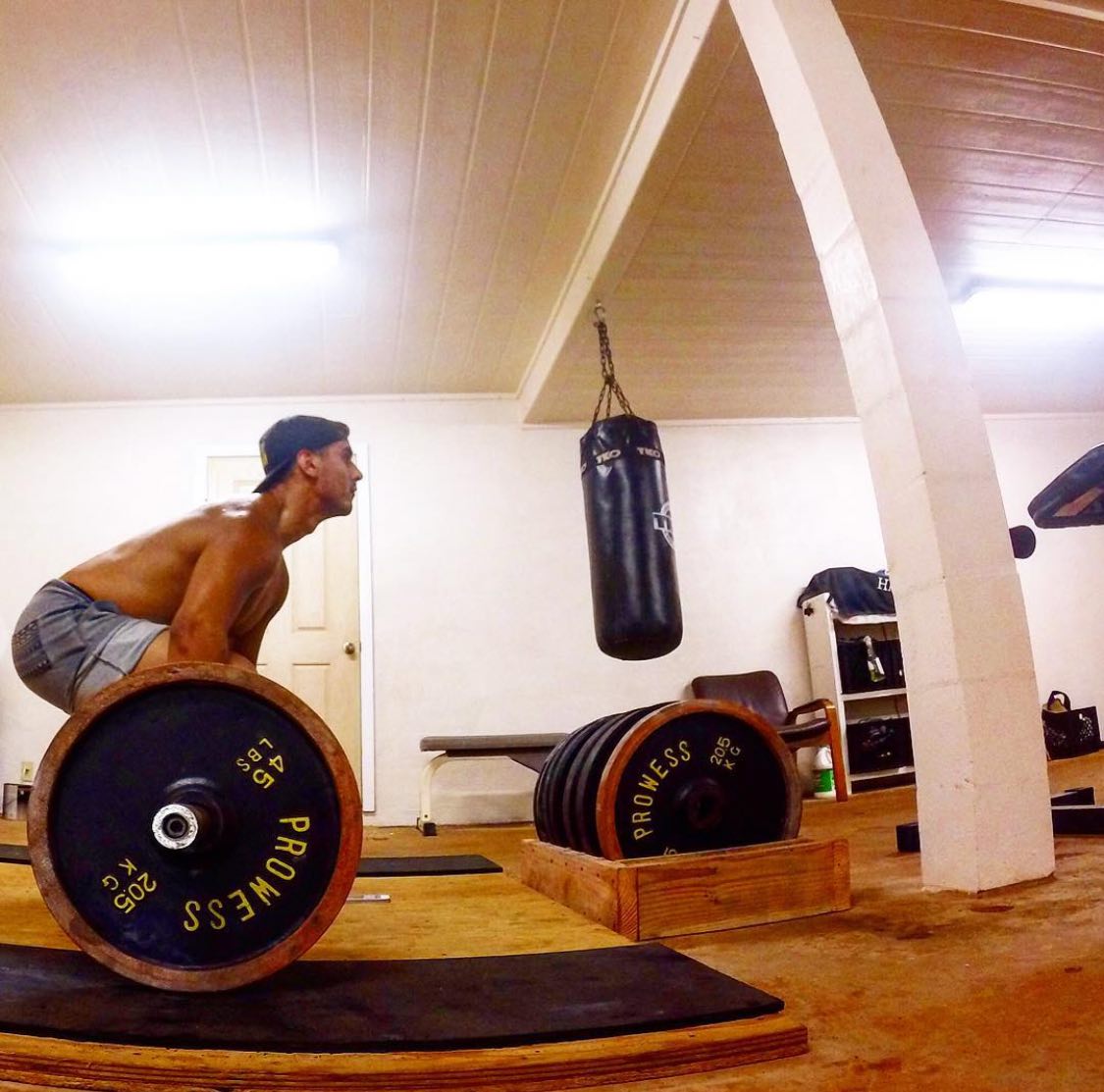 Ty set over a loaded barbell in a home gym, heavy bag hanging behind him
